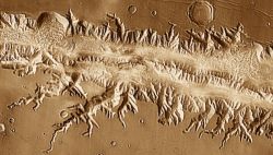 Valles Marineris (one part shown here) is the largest canyon in the solar system. Large than the Grand Canyon on Earth, Valles Marineris would stretch across the entire United States from California to New York. The tectonic activity which created the canyon — faulting and rifting — was likely caused by crustal stresses from the volcanic activity in Tharsis. (NASA/JPL-Caltech/Arizona State University)